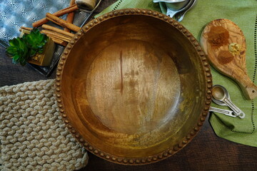 Empty wooden large mixing bowl surrounded by cinnamon sticks, pot holder, napkin and measuring cups.  Preparing to make a dessert .  Autumn or Fall flat lay with warm vibrant colors.  Wooden bowl.