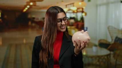 Woman smiling holding piggybank in stylish hotel lobby showcasing modern interior design and...