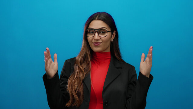 Woman gestures showing size in business attire against vibrant blue background exuding confidence and professionalism with long hair and glasses.