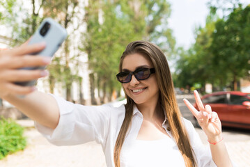 Attractive young woman in casual clothes and sunglasses taking a selfie photo on mobile phone...