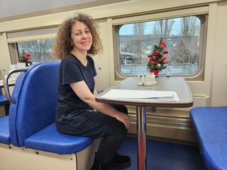 Woman sitting at a table in a train car. The table has a plate of food and a cup in train...