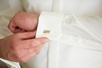 A man is getting ready to wear a white shirt and is adjusting his cuff. The shirt is white and has...