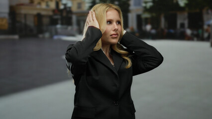 Blonde woman outdoors in city covering ears, expressing distress on urban street, surrounded by...
