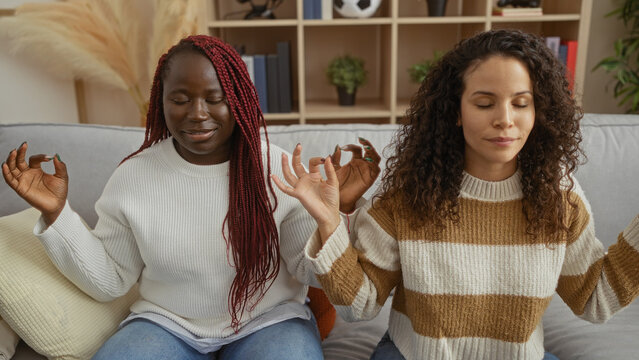 Women friends meditate peacefully together indoors in a cozy living room setting, reflecting a harmonious and serene environment for relaxation and personal connection.
