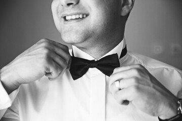 A man is getting ready to wear a black bow tie. He is smiling and he is in a good mood
