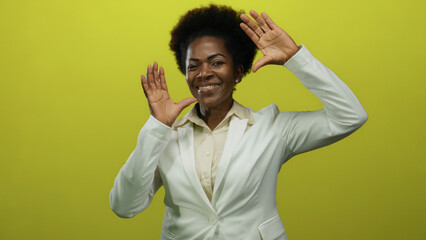 Woman smiling in white blazer over yellow background, expressing joy with raised hands in a studio...