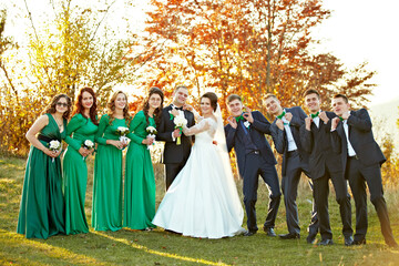 A group of people, including a bride and groom, are posing for a photo in a field. The bride is...