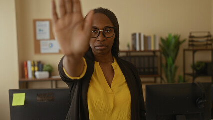 Woman with curly hair makes a stop gesture in an office setting, conveying professionalism and...