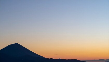 火山の山影が静かに佇み、右側には柔らかな夕焼け色が広がるマットな空が大きく開け、滑らかなグラデーションで穏やかな時間を描く風景写真
