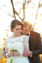 A bride and groom are embracing each other in a wedding photo. The bride is holding a bouquet of...