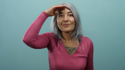 Woman with grey hair wearing pink sweater looking into the distance with hand above brows against a...