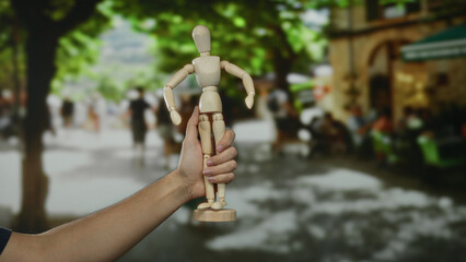Man holding wooden mannequin on bustling city street, blending art and people, showcasing a unique...