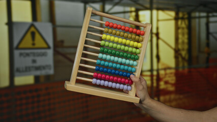 Caucasian man holding colorful abacus at a construction site with scaffolding in the background.