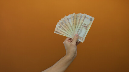 Male hand holding united arab emirates dirham banknotes against orange wall, showcasing currency...