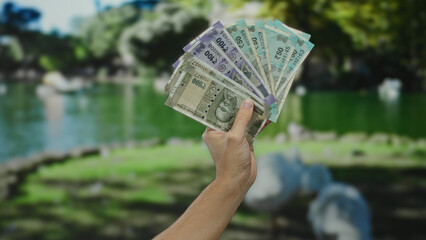 Caucasian man holding indian rupee banknotes in hand at a park demonstrating financial success in...