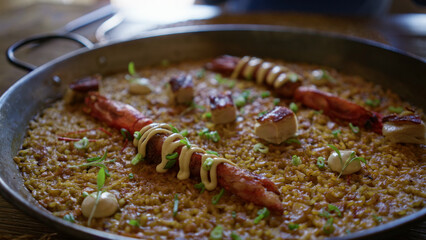 Delicious seafood paella decorated with mayonnaise and herbs served in a rustic mediterranean restaurant highlighting spanish gastronomy with rice and carabineros lobster.