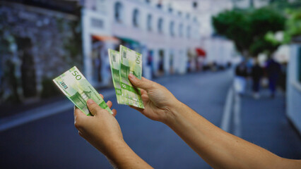 Hands holding norwegian kroner banknotes in an urban outdoor setting, suggesting business and...