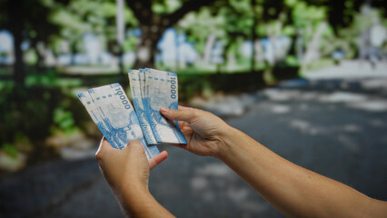 Man holding chilean pesos stands outdoors on a bright city street, highlighting urban finance,...