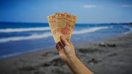 Hand holding mexican pesos near seaside in city setting evokes themes of money, investment, and...