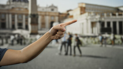 Man's hand points forward in vatican's san pedro square with people and historic architecture...