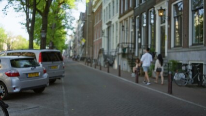 Blurred street scene with people walking in a european city, featuring trees, parked cars with dutch plates, bicycles, and historical architecture, capturing urban life and movement.