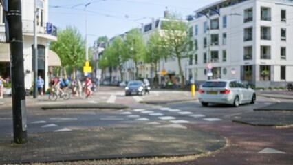 Blurred cityscape featuring cyclists and cars on a european intersection in a vibrant town, with people and modern buildings in the background creating a bokeh effect.