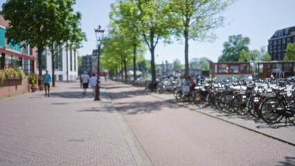 Defocused view of people walking along a tree-lined street in amsterdam with bicycles parked nearby, showcasing urban life in a vibrant city setting.