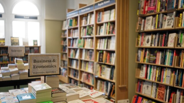 Blurred books and shelves create a vibrant library atmosphere indoors, with business and economics sections highlighted by soft focus and defocused background.