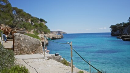 Blurred scenic view of cala llombards beach in mallorca with defocused turquoise water and rocky coastline under clear blue sky
