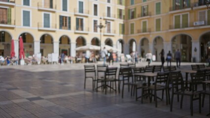 Chairs and tables in a european town square with blurred, defocused people and vibrant bokeh of cafes and buildings under the sun.