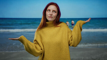 Woman with red hair and yellow sweater standing on beach with ocean in background, embodying peace and harmony amidst scenic seaside setting.
