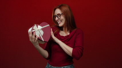 Woman smiling while holding heart shaped gift box against red background illustrating love and...