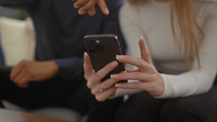Woman holding smartphone while man points at screen indoors, indicating modern lifestyle and technology use in comfortable home setting.