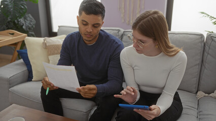 Woman using tablet while man reviews documents in a cozy living room setting, highlighting a collaborative moment indoors in a modern apartment atmosphere.