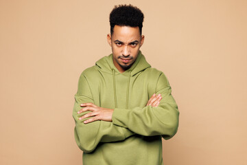 Young sad man of African American ethnicity wear green hoodie casual clothes hold hands crossed...