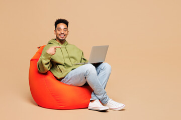 Full body young fun IT man of African American ethnicity wears green hoodie casual clothes hold use...