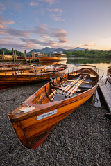 Wooden boats moored on Derwentwater shoreline at sunset on a calm summer evening. Lake District, UK.