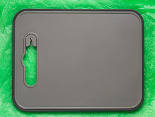 Gray plastic textured cutting board is on a crumpled plastic green background. Can be used as a backdrop for advertising. Flat lay. Copy space