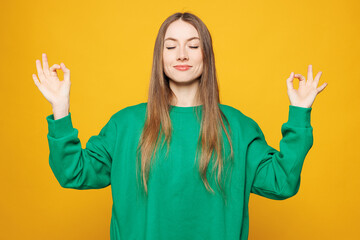 Young Caucasian woman she wear green sweatshirt casual clothes hold hands in yoga om aum gesture...