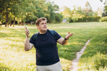 Sad blonde man got lost and could not find an internet connection on phone on the nature background. Male explorer looking for connection to the internet or using gps navigator app on phone