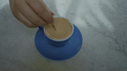 Hand stirring coffee in a blue cup on a countertop with a spoon in an indoor restaurant setting...