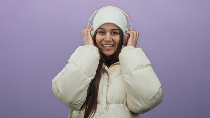 Young hispanic woman in a white coat and beanie listening to music with headphones on a vibrant...