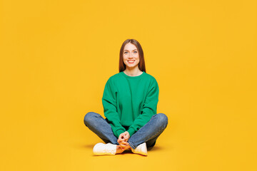 Full body young smiling happy cheerful fun cool woman she wear green sweatshirt casual clothes sitting look camera rest isolated on plain yellow orange background studio portrait. Lifestyle concept.