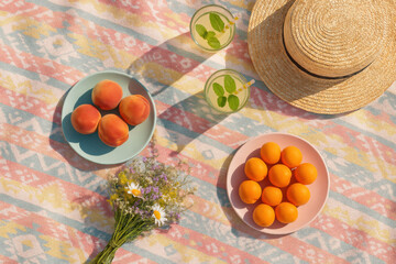 Summer picnic setting with fresh apricots, refreshing drinks and wildflowers on a colorful blanket