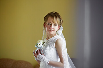 A woman in a wedding dress holding a bouquet of flowers. She is smiling and looking at the camera