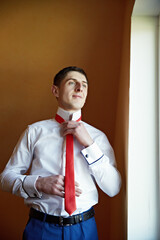 A man is getting ready to tie his red tie. He is smiling and looking at the camera