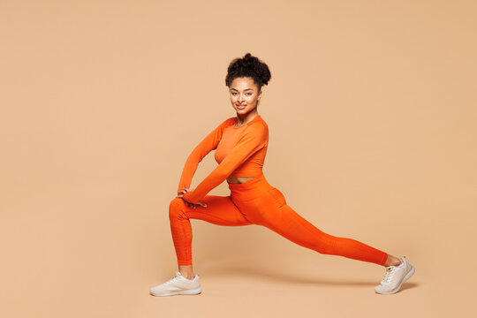 Full body young fitness trainer instructor sporty woman sportsman wears orange clothes spend time in gym do squat lunges stretch leg isolated on plain beige background. Workout sport fit abs concept - Powered by Adobe