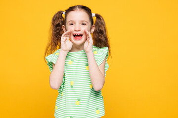 Little fun kid child girl 8-9 years old she wears green t-shirt sharing hot news about sales discount with hands near mouth isolated on plain yellow background. Mother's Day family lifestyle concept.