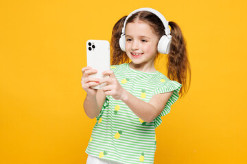 Little smiling cute kid child girl 8-9 years old wear green t-shirt listen to music in headphones...