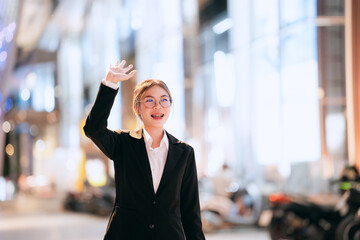 Confident young businesswoman in a black suit standing outdoors at night, smiling with arms...